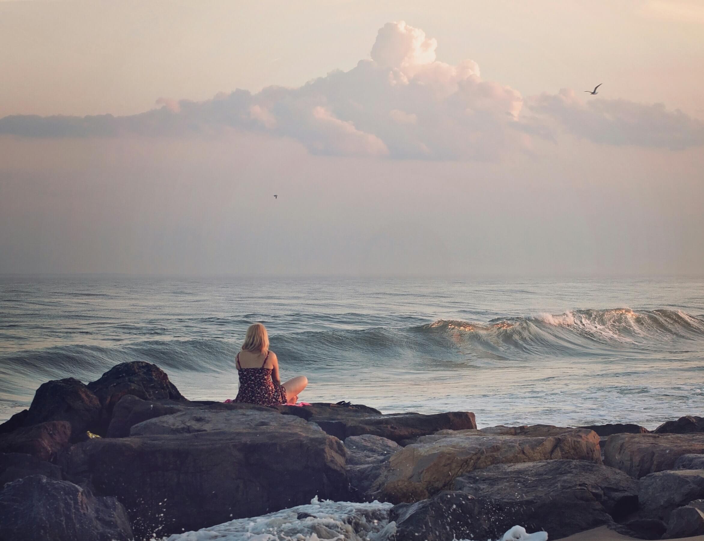 mujer rubia que está en las rocas frente al mar escribiendo un diario de agradecimientos